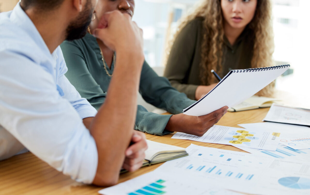 three people sitting at a table discussing a stack of papers in front of them